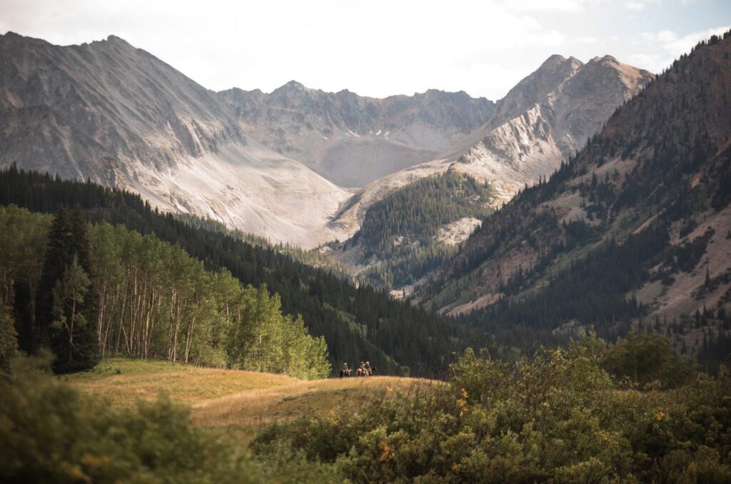 Horseback riders in a meadow below the Elk Mountains