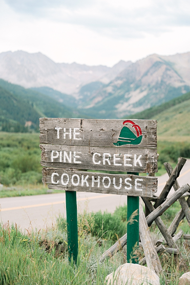 The Pine Creek Cookhouse wooden sign on Castle Creek Road with the Elk Mountains behind
